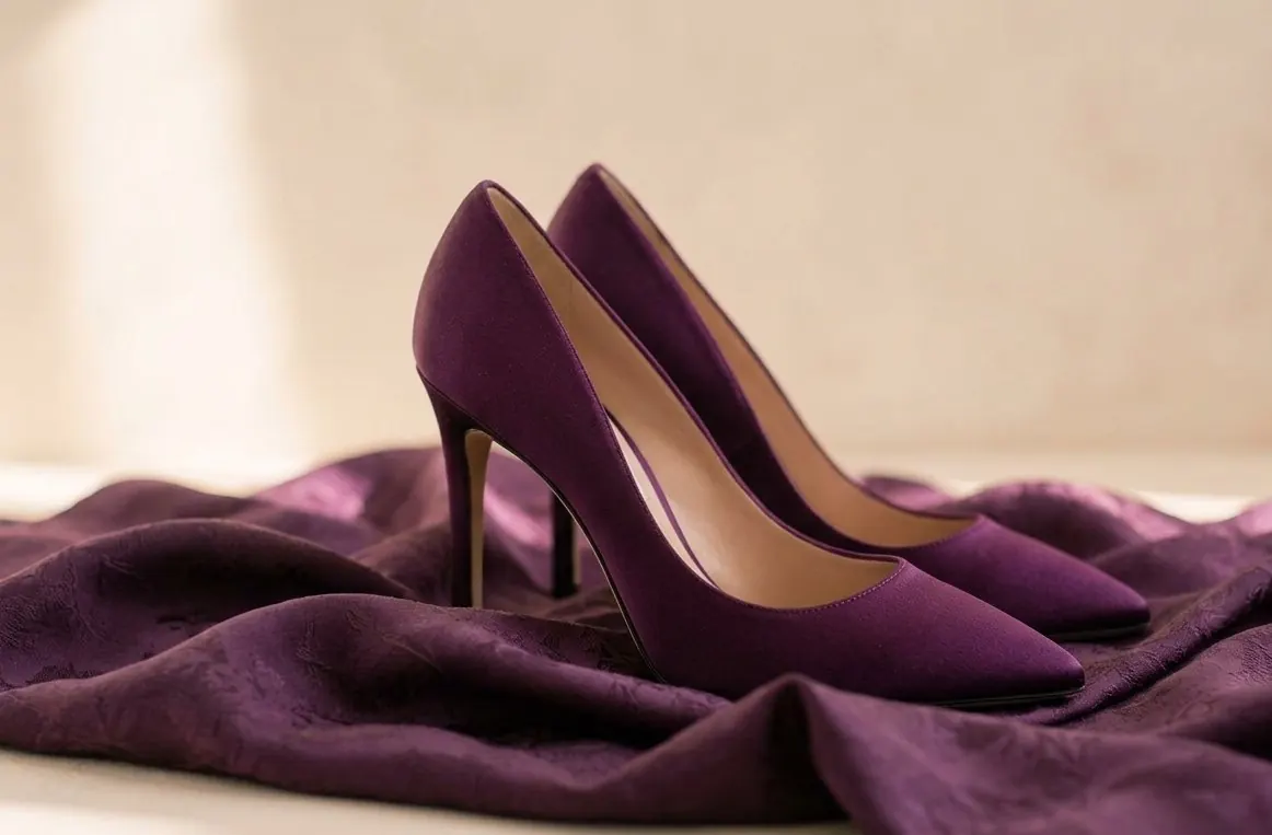 A pair of plum satin pumps resting on draped purple silk