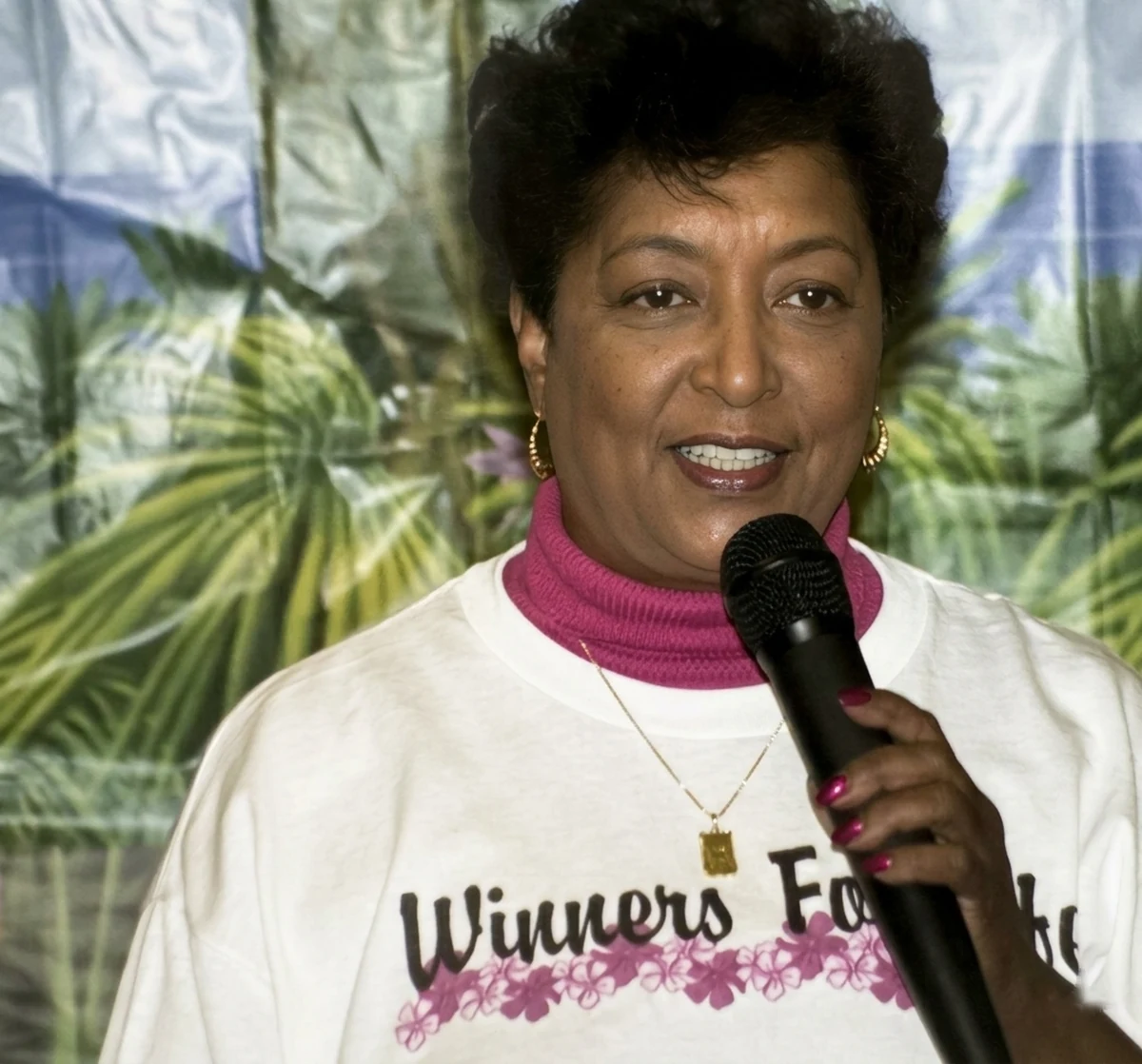 Dr. Winifred Frelow speaking into a microphone, wearing a Winners For Life shirt